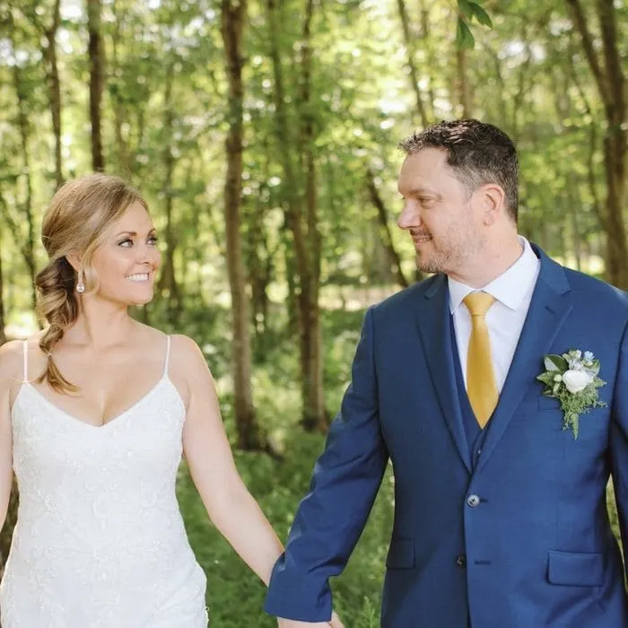 A bride and groom holding hands on a wooded path