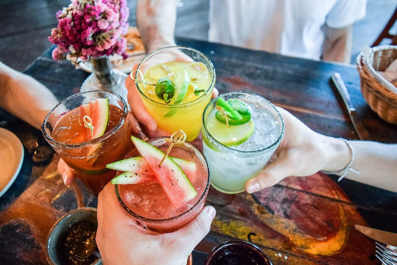 Friends raising colorful cocktails in a toast over a restaurant table